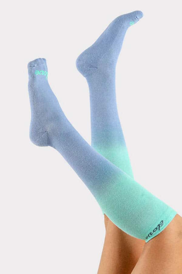 Give good: 9 charity gifts fashion enthusiasts will love 2 Close up of raised legs wearing green and blue compression socks from charity brand Clove.