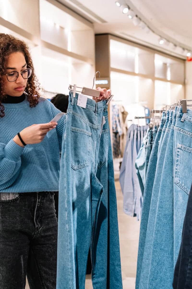 Cost per wear: How to maximize your clothing budget 2 Woman checks price tag of jeans to represent cost per wear concept.