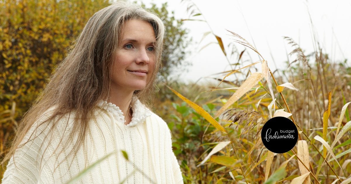 Mature woman wearing sweater outside near yellow and green foliage.
