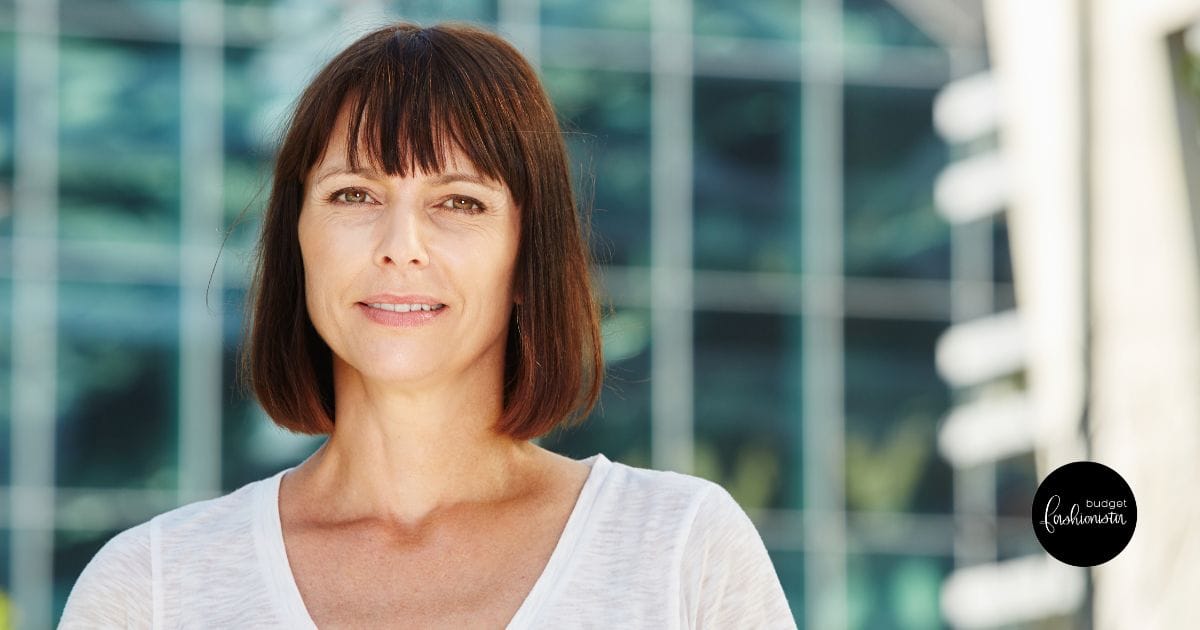 Woman with bob hair style and white top stands outside.