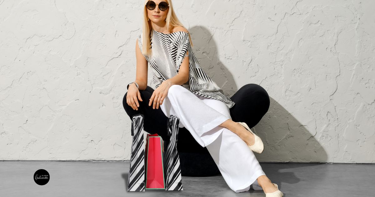Woman sitting wearing wide-legged pants with a striped bag.
