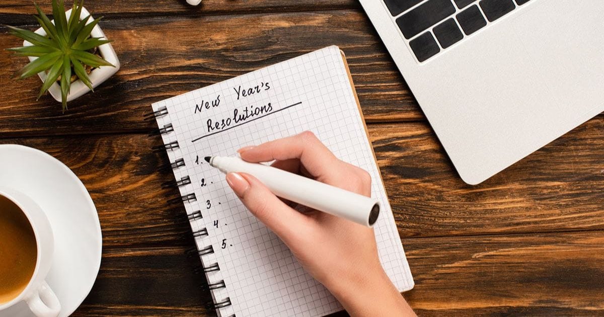 Close view of hand writing out New Year's resolutions in a spiral bound book.