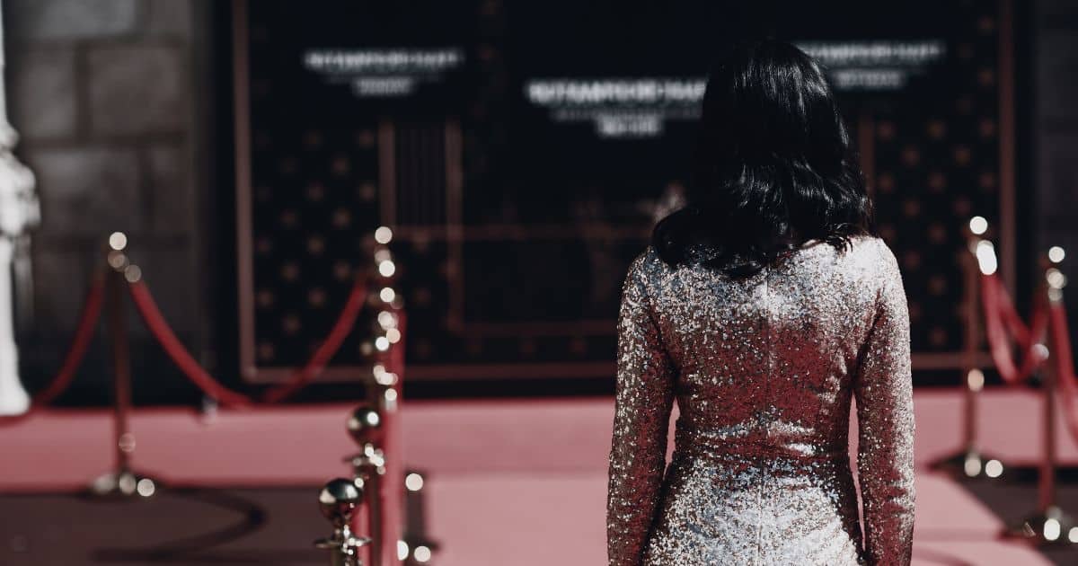 Low-saturation image of woman walking down a red carpet in a sequin dress.