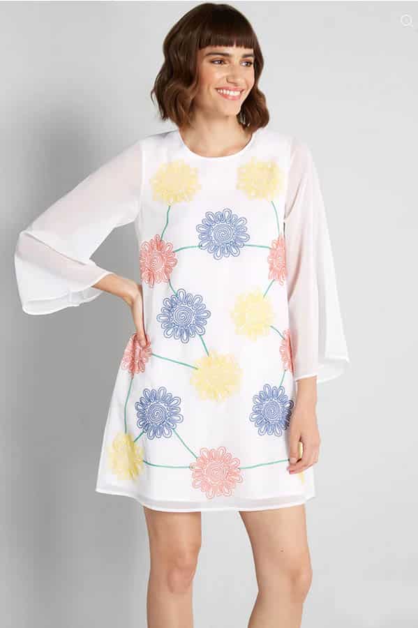Model wearing white dress with sheer sleeves.