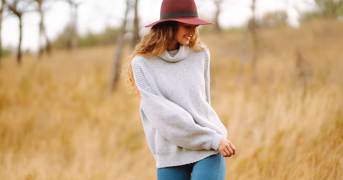 Woman smiling wearing sweater outside in field.