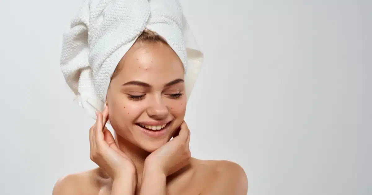 Smiling woman with acne wearing a towel on her head.
