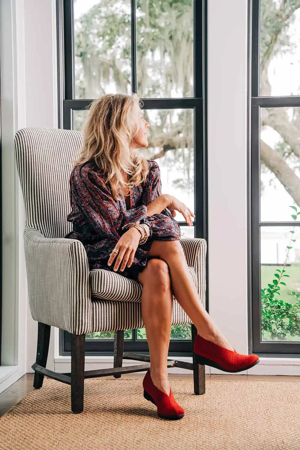 Woman sitting on chair inside wears red bunion-friendly shoes.