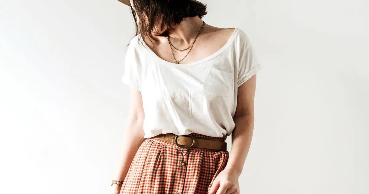 Model wears pleated pants and white top in front of white background.